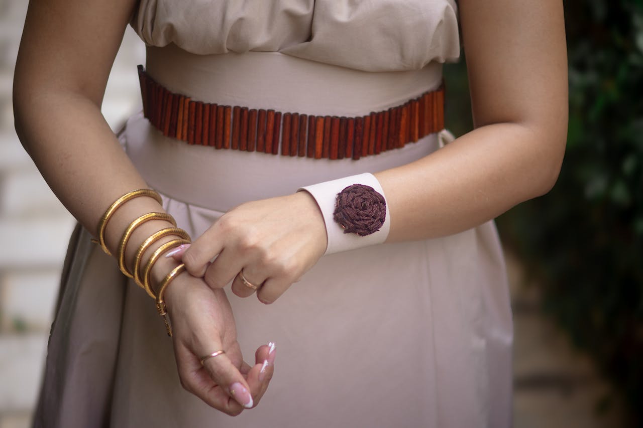 A close-up of an elegant woman wearing stylish bangles and a decorative belt outdoors.